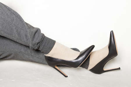 a young girl in gray sweatpants and black pointed toe high-heeled shoes stands on a white carpet at homeの写真素材