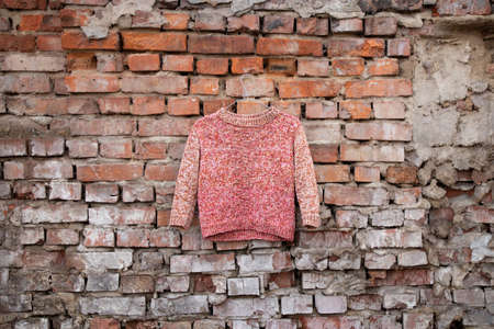 multicolored jacket in orange tones for women hangs on a brick old wall outside in the sun