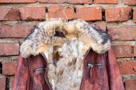 red fur leather winter women jacket hanging on a hanger on a brick old wall outdoors during the day, womens clothingの写真素材