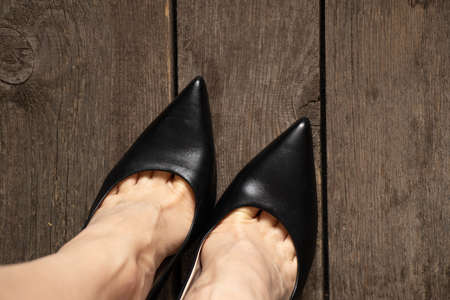 female legs in black leather high heel shoes on old wooden floor and burlap carpet, top to bottom viewの写真素材