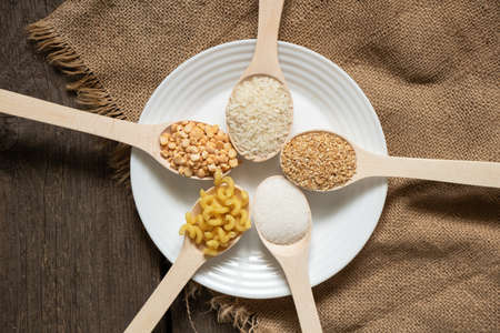 sugar rice peas pasta cereals on wooden spoons on the table on the kitchen, foodの写真素材