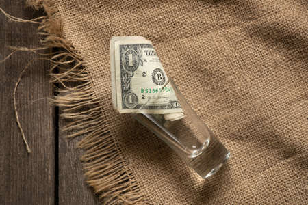 American dollar lies in a glass shot glass on an old wooden table on a tablecloth, money in a shot glassの写真素材
