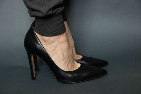 girl in gray sweatpants and leather shoes black high heels on isolated blue backgroundの写真素材