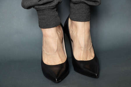 girl in gray sweatpants and leather shoes black high heels on isolated blue backgroundの写真素材