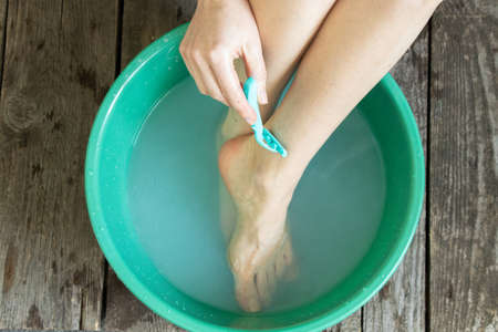 the girl washes her legs and shaves them with a tanok in a green bowl on the floor of the house