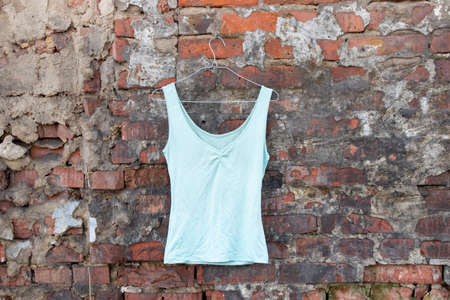 women's blue t-shirt hanging on a hanger on a brick wall in the street, women's clothingの写真素材