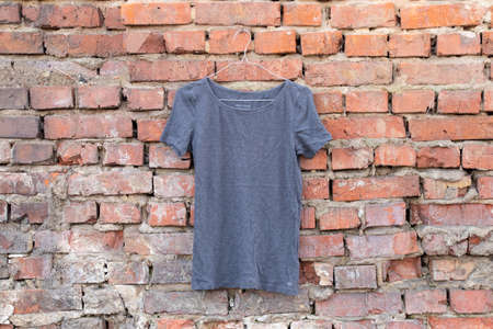 womens gray t-shirt hanging on a hanger on a brick wall in the street, womens clothingの写真素材