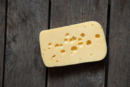 a piece of hard cheese on a wooden table close-upの写真素材