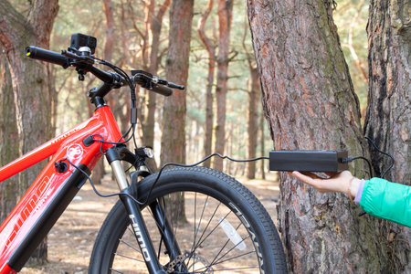Ukraine Dnipro 05.04.2021 - a red electric bike is recharged in a forest in a park, new technologies, an electric bikeのeditorial素材