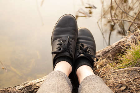 female legs in black leather shoes on the background of the river in spring on vacation in the forest, outdoor recreationの写真素材
