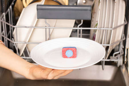 female hand holds on a plate a dishwashing tablet for a dishwasher on the background of dirty...