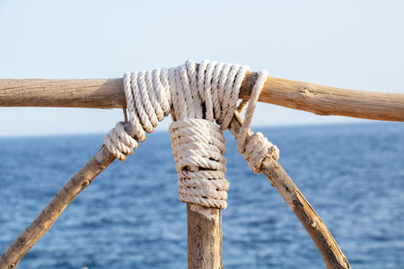 wooden railing wrapped with an old rope on the background of the sea in the sun