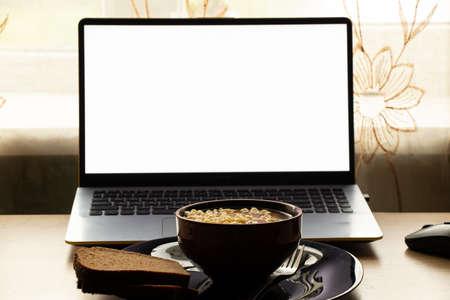 a plate of noodles stands next to a laptop with a white screen on the table in the room, the windows were taken, lunch at the desk at home, foodの写真素材