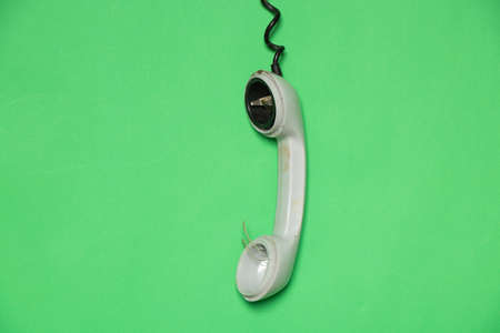old broken telephone receiver on wire weighs on green isolated background, telephone receiver on prododi brokenの写真素材
