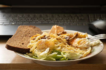 a plate with egg noodles and salad with a piece of black bread on the desktop at home they brought a laptop, lunch while working at the computer, working onlineの写真素材
