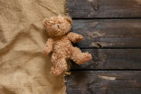 an old teddy brown bear lies alone on a charred wooden floor on a brown cloth, a child's toy on the floorの写真素材