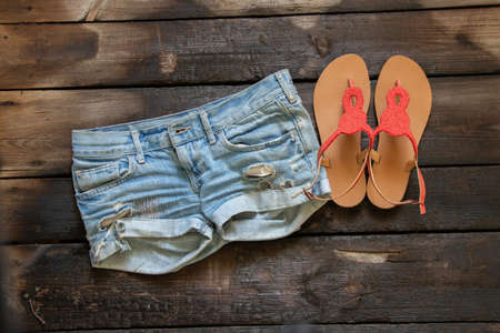 short denim women's shorts and summer sandals on an old wooden table, women's clothing and footwear, fashionの写真素材