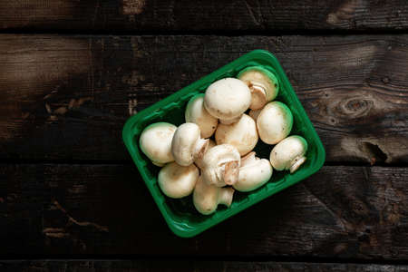 mushrooms champignons in a green plastic box on an old wooden table in the kitchen, raw bends from the storeの写真素材