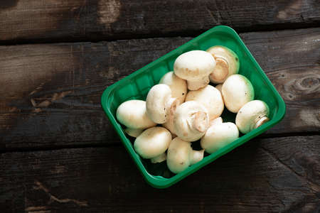mushrooms champignons in a green plastic box on an old wooden table in the kitchen, raw bends from the storeの写真素材