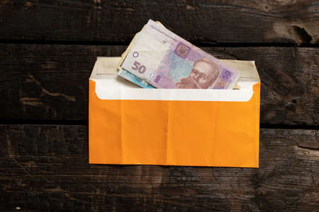 Ukrainian hryvnia in a yellow envelope on a wooden table, wages in an envelope, money in an envelopeの写真素材