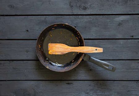 a frying pan with food leftovers and a wooden spatula after frying is on the table in the kitchen, a dirty frying pan is on the tableの写真素材