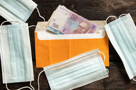 a medical mask lies in an envelope with Ukrainian money on a wooden table, money and a medical mask