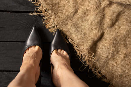 female legs in black high-heeled shoes on a black wooden floor and brown fabric, bottom view, women's shoesの写真素材