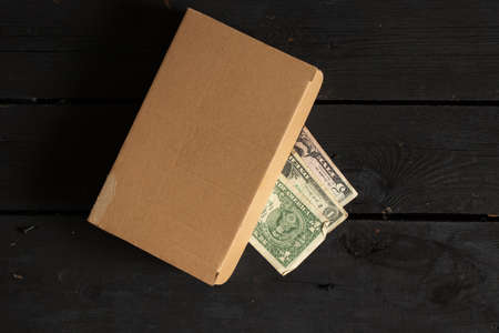 american dollars lie in a corton brown box on a black wooden table, money in a box on the tableの写真素材