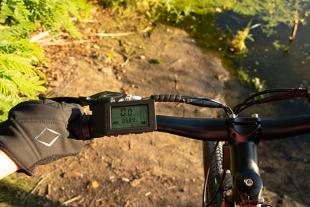 a female hand in a black glove holds the steering wheel of an e-bike in the sun in the park, driving an e-bike, resting on a bikeの写真素材