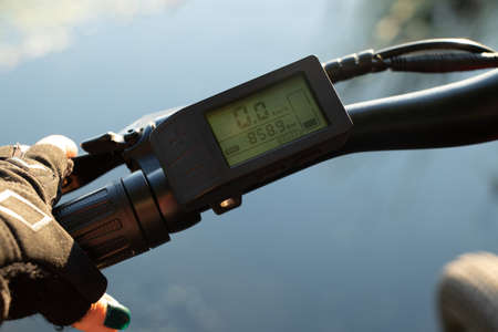a female hand in a black glove holds the steering wheel of an e-bike in the sun in the park, driving...