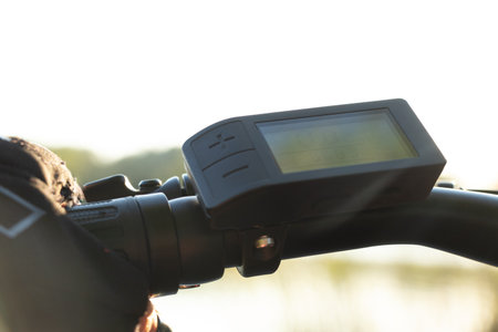 a female hand in a black glove holds the steering wheel of an e-bike in the sun in the park, driving an e-bike, resting on a bikeの写真素材