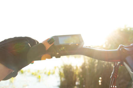 a female hand in a black glove holds the steering wheel of an e-bike in the sun in the park, driving an e-bike, resting on a bikeの写真素材