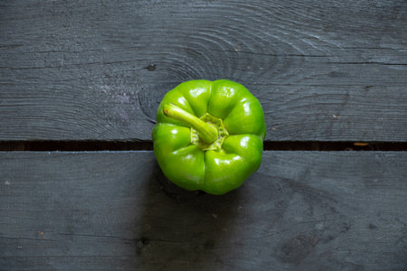 green raw whole bell pepper lies on a black wooden table, green pepper
