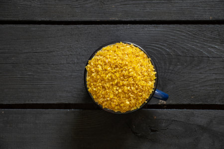 raw bulgur groats in a cup on a black wooden table, porridge in a cup