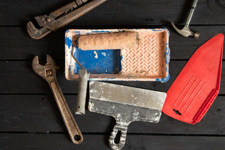 gas wrench hammer roller in paint in a tray and a spatula lie on a black wooden floor, repair tools,...