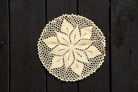 crocheted lace doily lies on a black wooden table, doily on the tableの写真素材