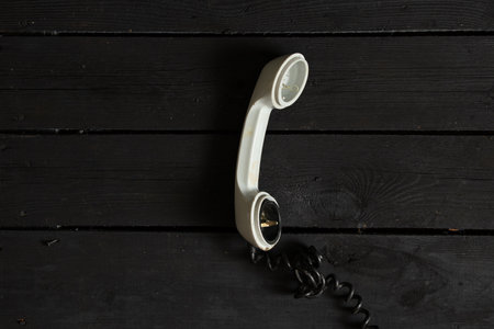 an old broken plastic telephone receiver with a wire lies on a black wooden table, phone call, communicationの写真素材