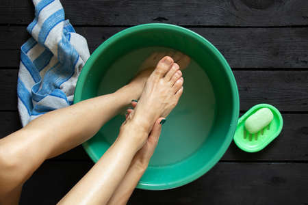 girl washes her feet in a bowl of water on the wooden floor at home, foot care, wash feet at home, hygieneの写真素材