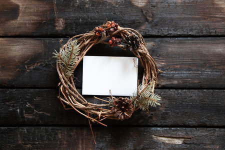 new year christmas wreath and in the center a white paper card for text on an old wooden table, decor for the holiday, a wreath from a dry vine, a place for textの写真素材