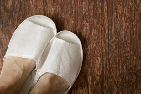 female feet in white slippers on brown wooden floor, feet on the floor at homeの写真素材