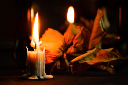 burning candle near the mirror on the table and next to it lies a dry rose in the dark, candle flame...