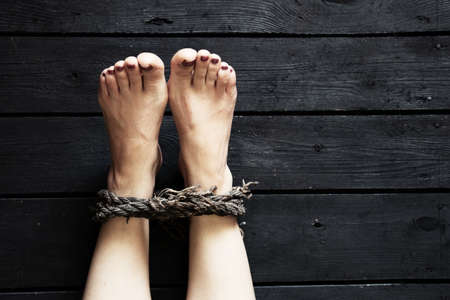 leg binding with old rope of a young girl on the black floor, human trafficking, slavery, no will