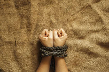 tied female hands by an old rope on brown cloth, tied hands, bondageの写真素材