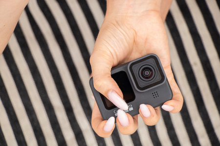 Ukraine Dnipro 08/05/2021 - Camera GoPro HERO 9 female hand holds on a striped background on the beach, action camera in handsのeditorial素材