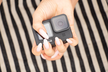 Ukraine Dnipro 08/05/2021 - Camera GoPro HERO 9 female hand holds on a striped background on the beach, action camera in handsのeditorial素材
