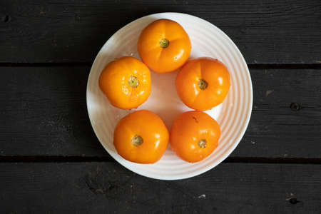 yellow tomatoes lie on a white plate on a black wooden table in the kitchen, ripe yellow tomatoesの写真素材