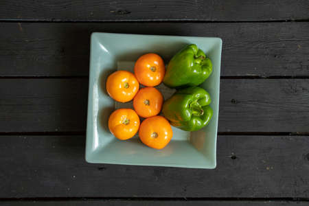 yellow tomatoes and selenium bell peppers lie on a plate on a black wooden table in the kitchen, ripe yellow tomatoes and peppersの写真素材