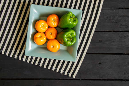 yellow tomatoes and selenium bell peppers lie on a plate on a black wooden table in the kitchen, ripe yellow tomatoes and peppersの写真素材