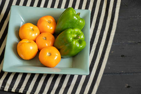yellow tomatoes and selenium bell peppers lie on a plate on a black wooden table in the kitchen, ripe yellow tomatoes and peppersの写真素材