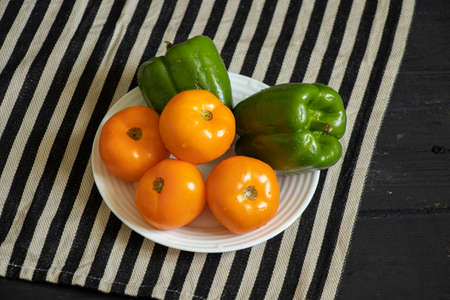 yellow tomatoes and selenium bell peppers lie on a plate on a black wooden table in the kitchen, ripe yellow tomatoes and peppersの写真素材